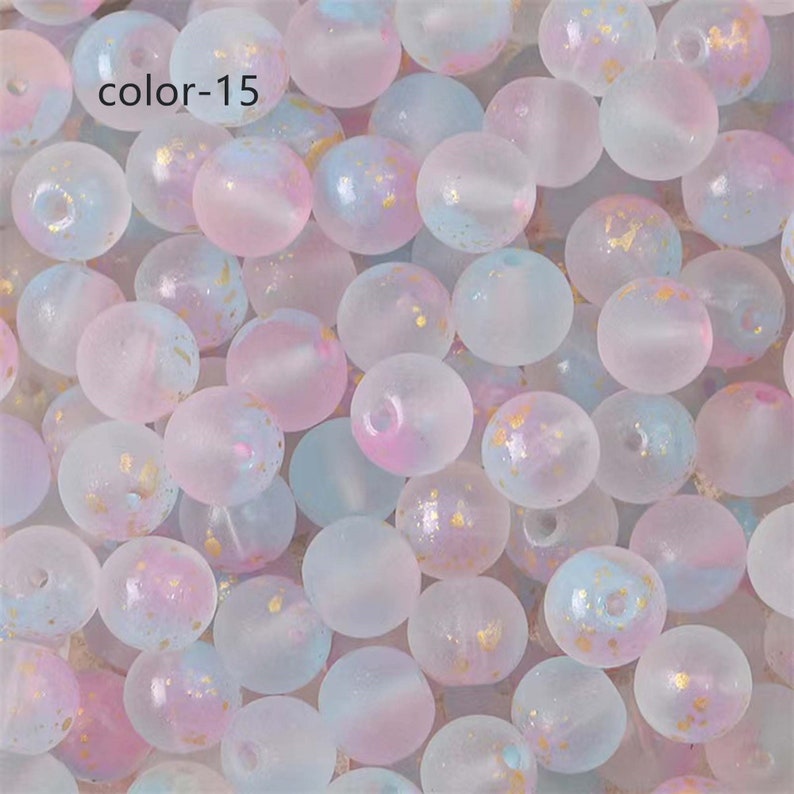 May include: A close-up of a collection of translucent, round beads with a frosted finish. The beads are a mix of light blue, pink, and white with flecks of gold glitter. The beads are labeled "color-15".
