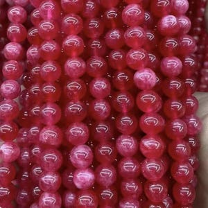 May include: A strand of bright pink round beads made of natural stone. The beads are smooth and have a slightly translucent appearance.