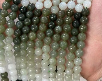 May include: Strands of round jade beads in varying shades of green and white. The beads are smooth and polished, with a slight sheen. The beads are strung together, creating a necklace or bracelet.