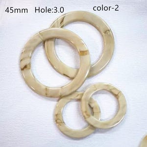 Puede incluir: Cuatro anillos circulares beige con un patrón veteado. Los anillos varían en tamaño, el más grande mide 4,5 cm de diámetro. El texto "45mm Hole:3.0 color-2" es visible en la esquina superior izquierda.
