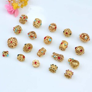 May include: Assortment of gold-tone metal beads with intricate designs and colorful gemstones. The beads feature a variety of shapes, including round, cylindrical, and flower-shaped.