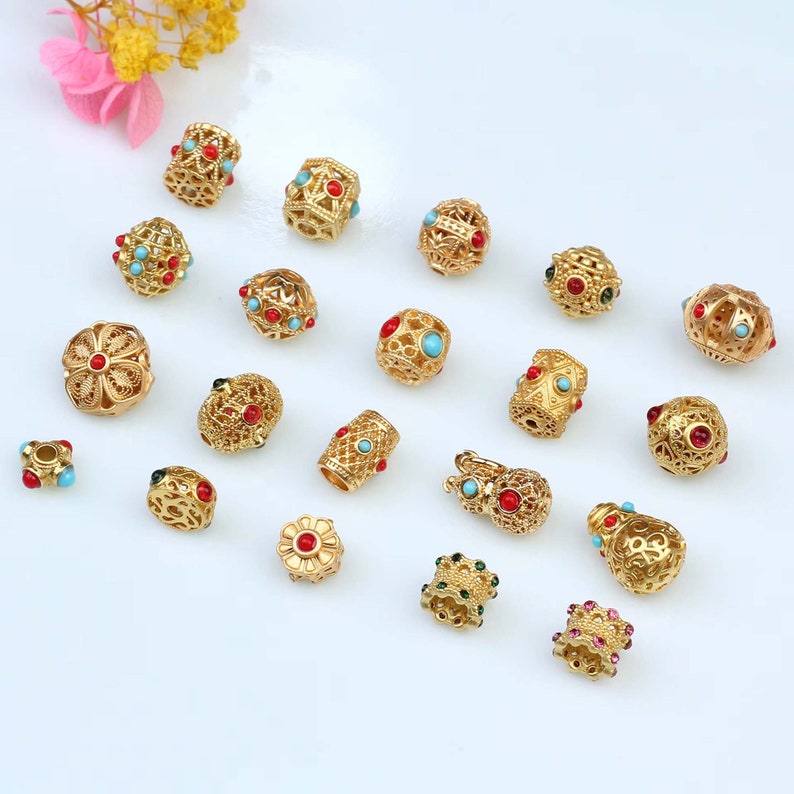 May include: Assortment of gold-tone metal beads with intricate designs and colorful gemstones. The beads feature a variety of shapes, including round, cylindrical, and flower-shaped.