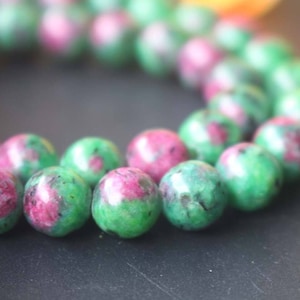 Puede incluir: Una hebra de cuentas de piedras preciosas verdes y rosas. Las cuentas son redondas y tienen un acabado liso y pulido.