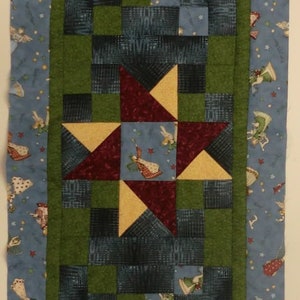 May include: A green, blue and red patchwork quilt runner with a star pattern. The runner has a blue border with a white and blue floral pattern.