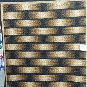 May include: A quilt with a brown and beige striped pattern. The stripes are arranged in a diagonal pattern, creating a sense of movement. The quilt is made of a soft, textured fabric.