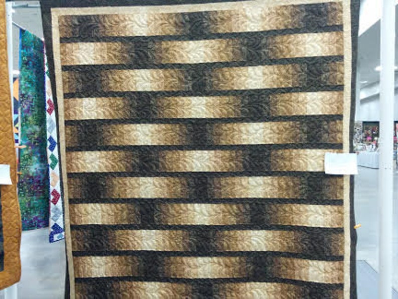 May include: A quilt with a brown and beige striped pattern. The stripes are arranged in a diagonal pattern, creating a sense of movement. The quilt is made of a soft, textured fabric.