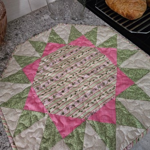 May include: A pink, green and beige quilted table runner with a starburst pattern. The centre of the runner features a pink and green striped fabric with a floral design.