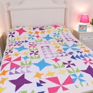 May include: A white bed with a colourful quilt featuring stars, pinwheels, and other geometric shapes in shades of pink, blue, green, purple, and yellow.