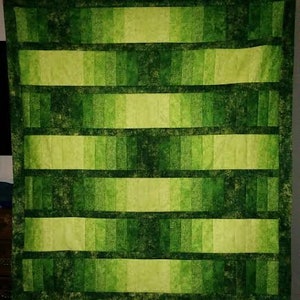 May include: A green and yellow ombre quilt with a checkered pattern. The quilt is made of fabric squares sewn together to create a gradient effect.