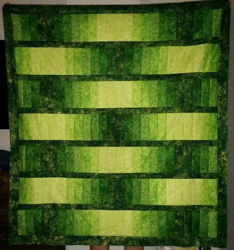 May include: A green and yellow ombre quilt with a checkered pattern. The quilt is made of fabric squares sewn together to create a gradient effect.