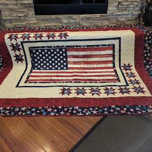 May include: A red, white, and blue quilt with a large American flag design in the center. The quilt is surrounded by a border of stars and stripes.
