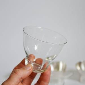 Peut inclure: Un verre en verre transparent avec un bord large et &eacute;vas&eacute; et une base &eacute;troite. Le verre est tenu dans une main, et deux autres verres sont flous en arri&egrave;re-plan.