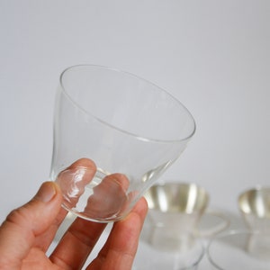 Peut inclure: Une tasse en verre transparent avec un bord large et &eacute;vas&eacute; et une base &eacute;troite. La tasse est tenue dans une main, et il y a deux autres tasses en arri&egrave;re-plan.