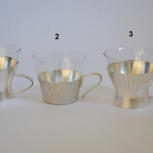 Peut inclure: Trois tasses en verre plaqu&eacute;es argent avec des poign&eacute;es. Les tasses sont num&eacute;rot&eacute;es 1, 2 et 3. Les tasses ont des motifs diff&eacute;rents sur le placage argent.