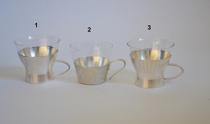 Peut inclure: Trois tasses en verre plaqu&eacute;es argent avec des poign&eacute;es. Les tasses sont num&eacute;rot&eacute;es 1, 2 et 3. Les tasses ont des motifs diff&eacute;rents sur le placage argent.