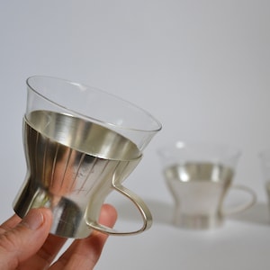 Peut inclure: Ensemble de trois tasses en verre plaqu&eacute; argent avec un motif cannel&eacute;. Les tasses ont un corps en verre transparent et un bord et une poign&eacute;e plaqu&eacute;s argent.