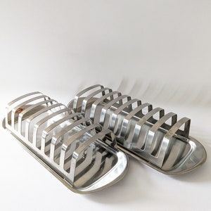 Puede incluir: Dos estantes para pan de metal plateado con forma rectangular y borde elevado. Los estantes tienen múltiples ranuras para sostener el pan.