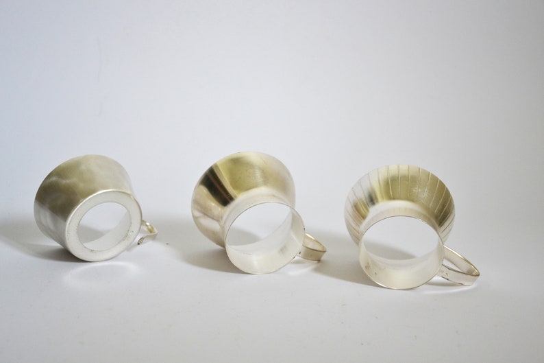 Peut inclure: Trois tasses en argent avec diff&eacute;rentes finitions. Les tasses sont toutes de la m&ecirc;me forme, mais l'une a une finition lisse, l'autre une finition martel&eacute;e et la derni&egrave;re une finition c&ocirc;tel&eacute;e.