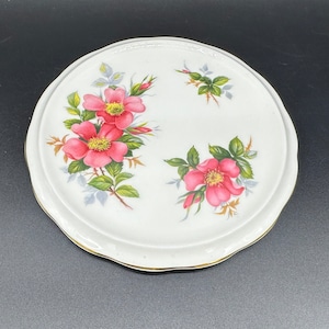 Puede incluir: Posavasos de cerámica blanca con borde dorado y diseño floral con rosas rosas y hojas verdes.