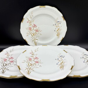 May include: Set of five white porcelain dinner plates with gold trim and floral designs. The plates feature delicate pink and blue flowers with green stems and leaves.