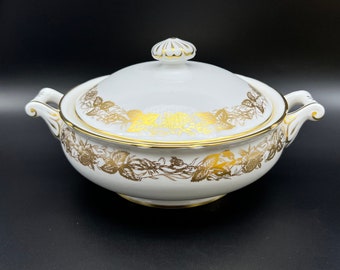 Może przedstawiać: Biała porcelanowa miska do serwowania z pokrywką, ozdobiona złotym wzorem kwiatowym. Miska ma dwa uchwyty i złotą obwódkę.