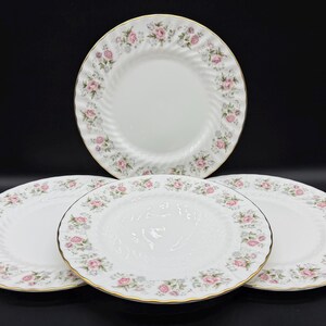 May include: Four white porcelain plates with a floral rose pattern and gold trim. The plates have a spiral design and are decorated with pink and green roses. A classic and elegant dinnerware set.