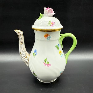 May include: A white porcelain coffee pot with a green handle and a floral design. The lid features a pink rose with green leaves.