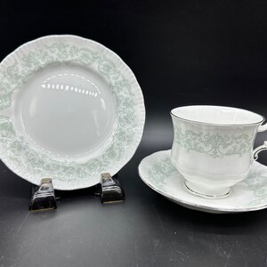 Könnte beinhalten: Ein weißes Tee-Set mit grünem Blumenmuster. Die Untertasse hat einen gewellten Rand.