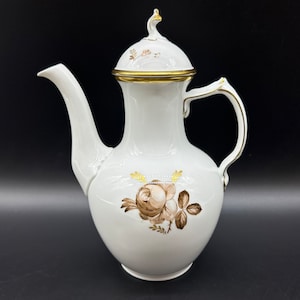 May include: White porcelain coffee pot with a gold trim and a brown rose design. The pot has a lid with a knob on top.