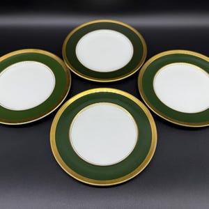 Puede incluir: Cuatro platos de cerámica blanca con un borde verde y dorado. Los platos están dispuestos en círculo sobre una superficie negra.