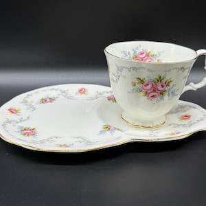 Puede incluir: Un juego de taza y platillo de té blanco con un patrón floral. La taza tiene un asa y el platillo tiene un borde festoneado.