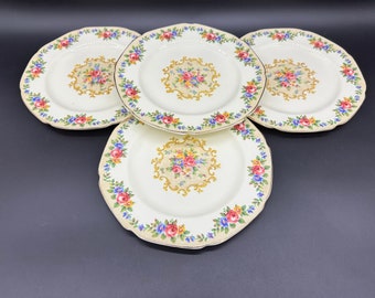 May include: Set of four vintage floral patterned dinner plates. The plates are white with a gold trim and feature a floral design with pink, blue, and yellow flowers.