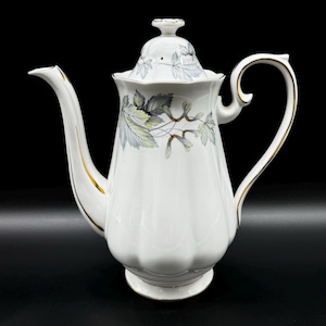 Puede incluir: Cafetera de porcelana blanca con ribete dorado y diseño floral. La cafetera tiene una tapa con un pomo en la parte superior.