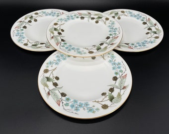 May include: Set of four white ceramic dinner plates with a gold rim and a floral design featuring blue flowers, green leaves, and brown berries.