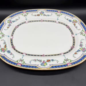 Pode incluir: Travessa oval para servir com centro branco e borda decorativa. A borda apresenta um design azul, preto e dourado com detalhes florais e de rolagem. A travessa tem uma borda dourada.