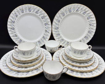 May include: A set of white teacups and saucers with a delicate floral pattern in shades of blue and purple. The set includes six teacups and saucers, and two larger plates with the same floral pattern.