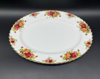 Può includere: Un piatto da portata ovale bianco con bordo dorato e un motivo floreale con rose rosse, gialle e verdi.