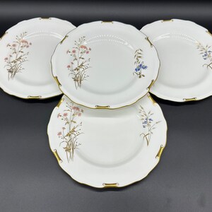 May include: Three white ceramic plates with gold trim and a floral design. The plates feature a delicate pattern of pink, blue, and brown flowers and leaves.