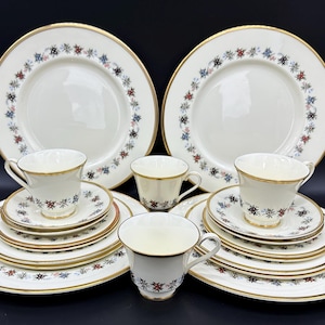May include: A set of white china dinnerware with a gold rim and a floral pattern in shades of blue, red, and black. The set includes two dinner plates, two salad plates, two teacups, and two saucers.