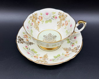 May include: A white teacup and saucer with a floral design and gold accents. The cup has a green interior and a gold floral pattern. The saucer has a white background with a gold floral pattern.