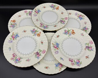 May include: Set of six white porcelain dinner plates with a floral pattern in shades of pink, blue, yellow, and orange. The plates have a scalloped edge and a gold trim.