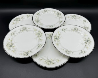 May include: Set of six white porcelain salad plates with a delicate floral design in shades of green and black. The plates have a black rim and a subtle sheen.