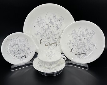 May include: A set of white ceramic dinnerware with a silver floral design. The set includes a large dinner plate, a salad plate, a saucer, and a teacup.