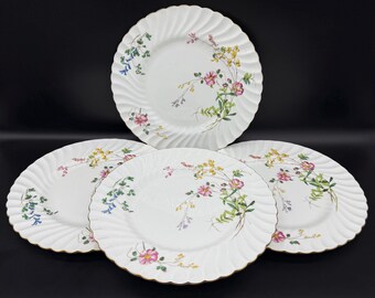 May include: Set of four white ceramic dinner plates with a floral design featuring pink, yellow, and blue flowers. The plates have a scalloped edge and a gold trim.