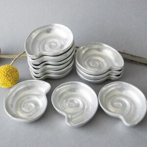 May include: A set of eight silver-colored metal dishes with a spiral design. The dishes are shaped like seashells and are stacked in a pile.