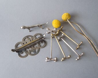 May include: A set of five silver and gold decorative stands with a round top and three legs. The stands are arranged in a fan shape. Two yellow dried flowers are in the background.