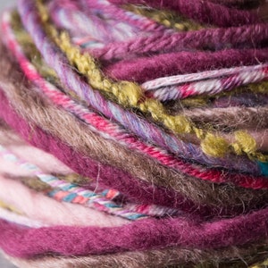May include: A close-up of a ball of yarn with multiple colors, including pink, brown, red, green, and purple. The yarn is soft and fluffy, and it appears to be hand-spun.