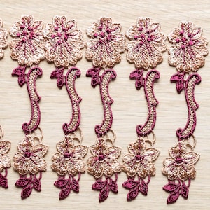 May include: Close-up of several embroidered floral appliques. The appliques feature a gold and burgundy color scheme. The floral designs are arranged in a repeating pattern, with a detailed, textured appearance. These appliques are suitable for various craft projects.