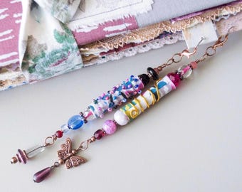 May include: Two beaded bookmark charms with copper-colored accents. One features a butterfly charm and a teardrop bead. The other has a white and gold wrapped design. Both have colorful beads.