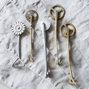 Può includere: Cinque diversi tagliapasta in metallo con vari disegni. I tagliapasta sono di colore argento e oro e hanno ruote di forme diverse.